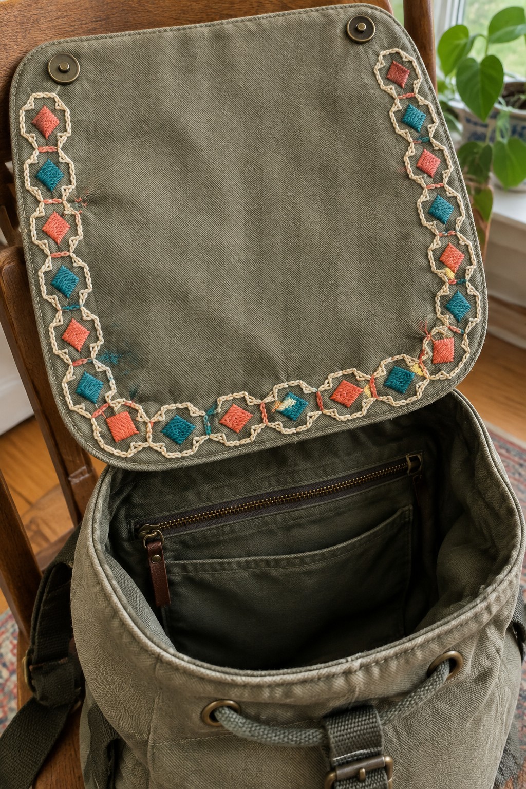 An open olive-green backpack has a coral and teal geometric embroidery border around its flap.