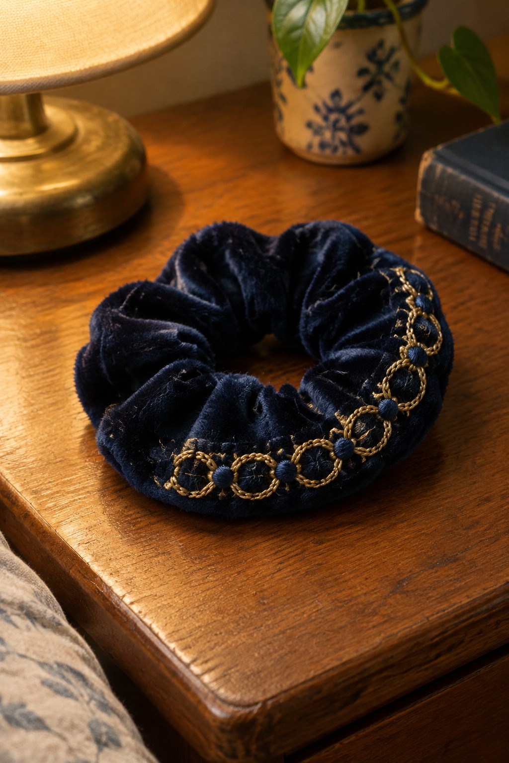 Navy velvet scrunchie with a gold interlocking-loop border and navy accents on a wooden table.