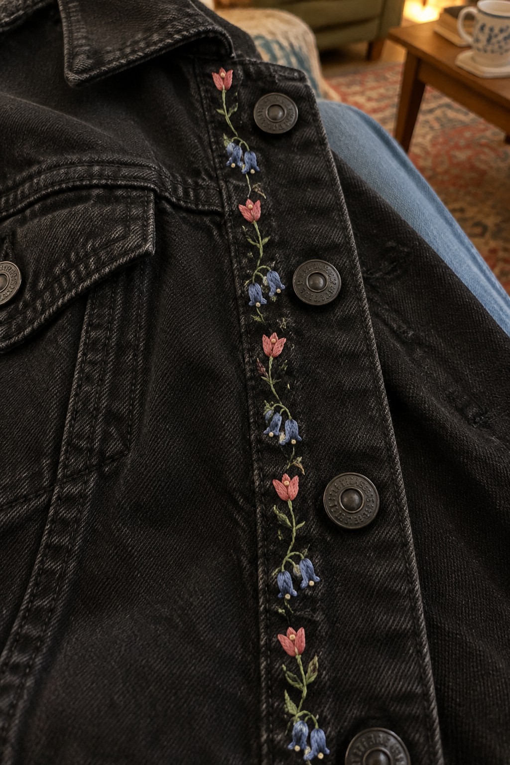 Pink and blue floral embroidery runs down the button placket of a black denim jacket.