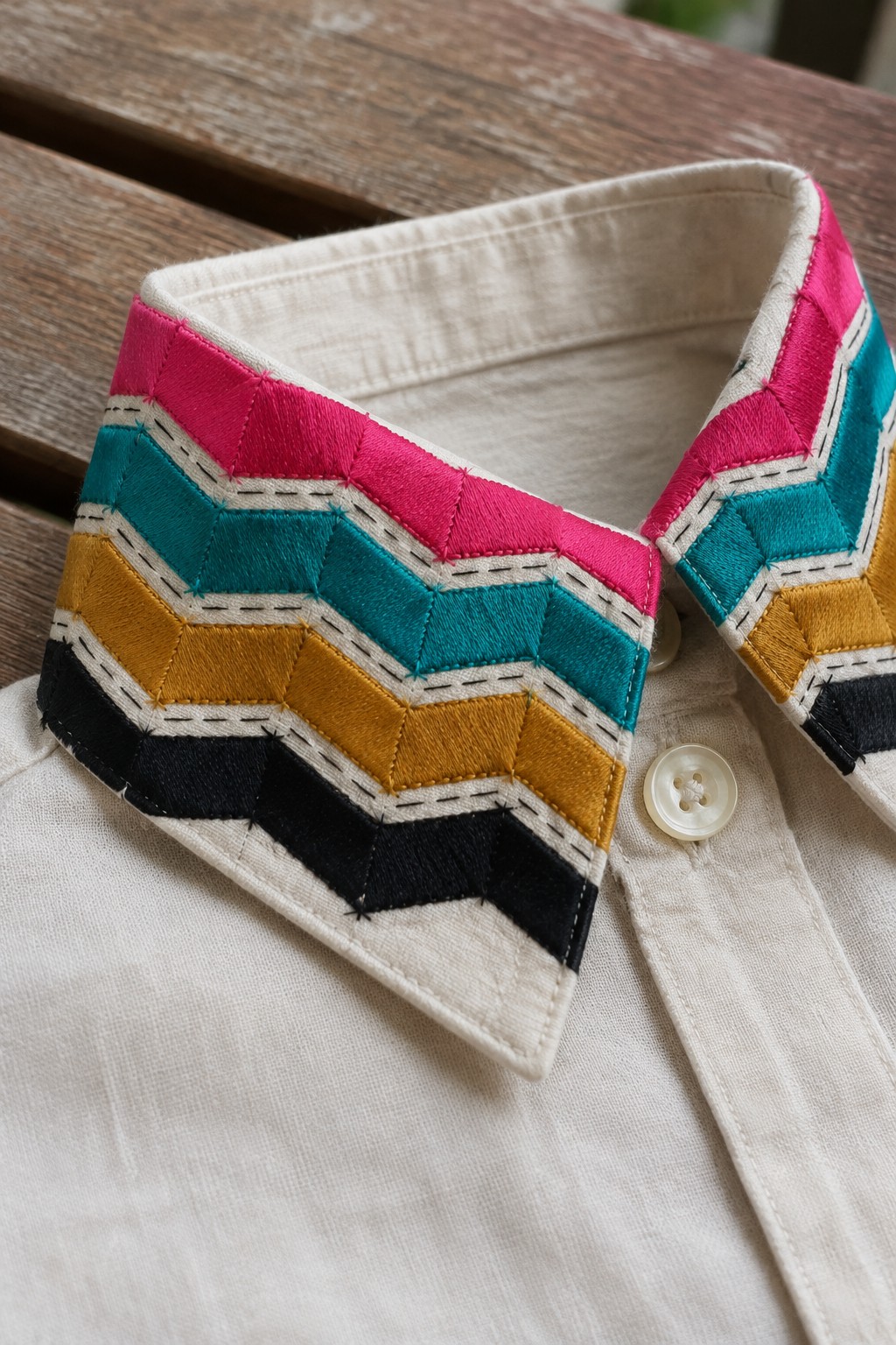 A beige shirt collar embroidered with rows of pink, teal, ochre, and black chevrons.