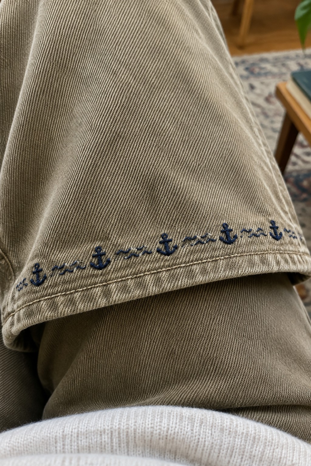 Navy anchors and wavy lines embroidered in a repeating border along the hem of khaki trousers.
