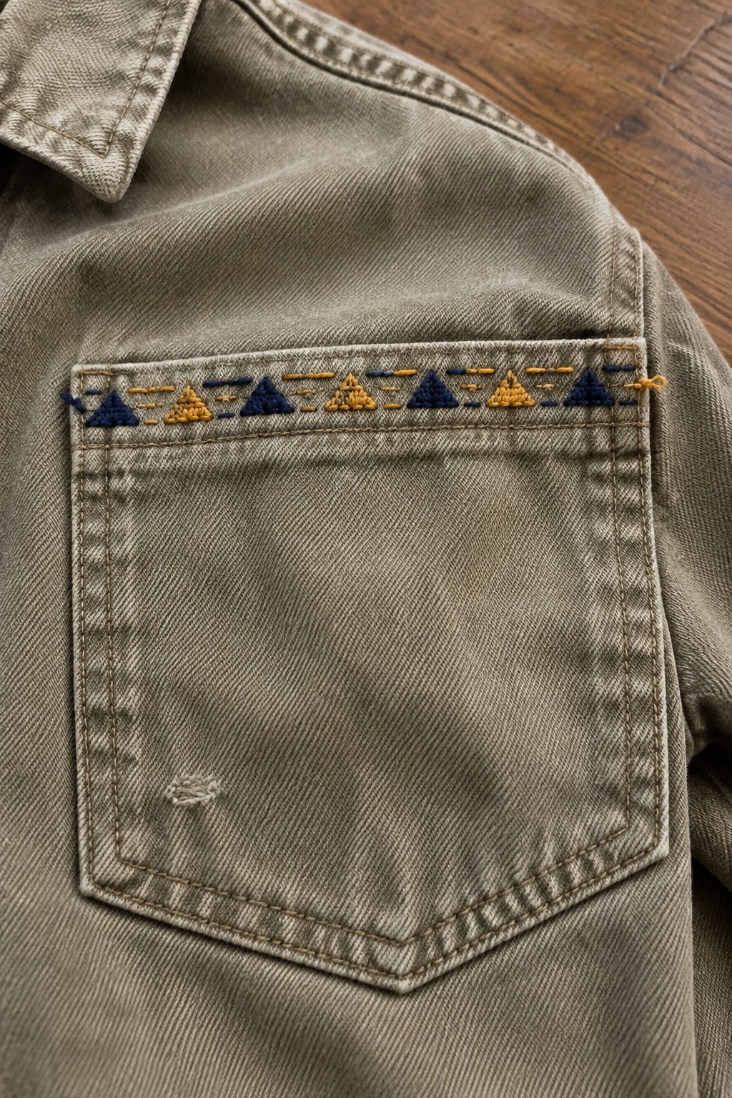 A denim jacket pocket embroidered with a row of alternating blue and golden triangles.