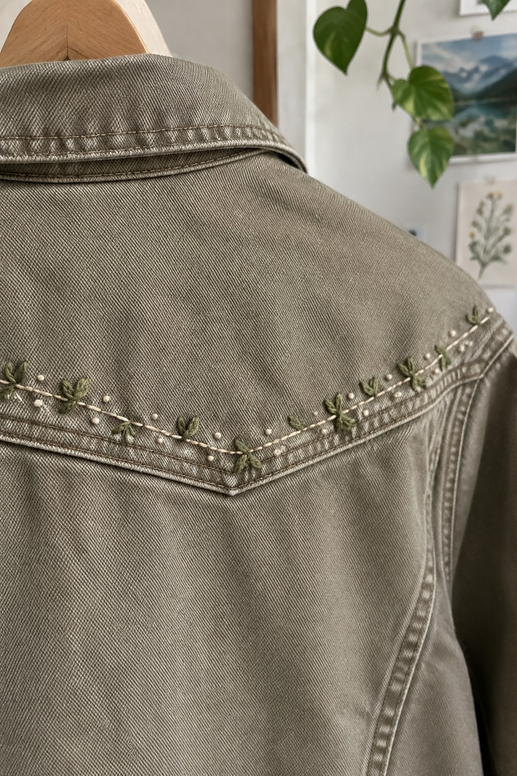 Green leaf embroidery and pale dots follow the angled yoke seam on the back of an olive-gray denim jacket.