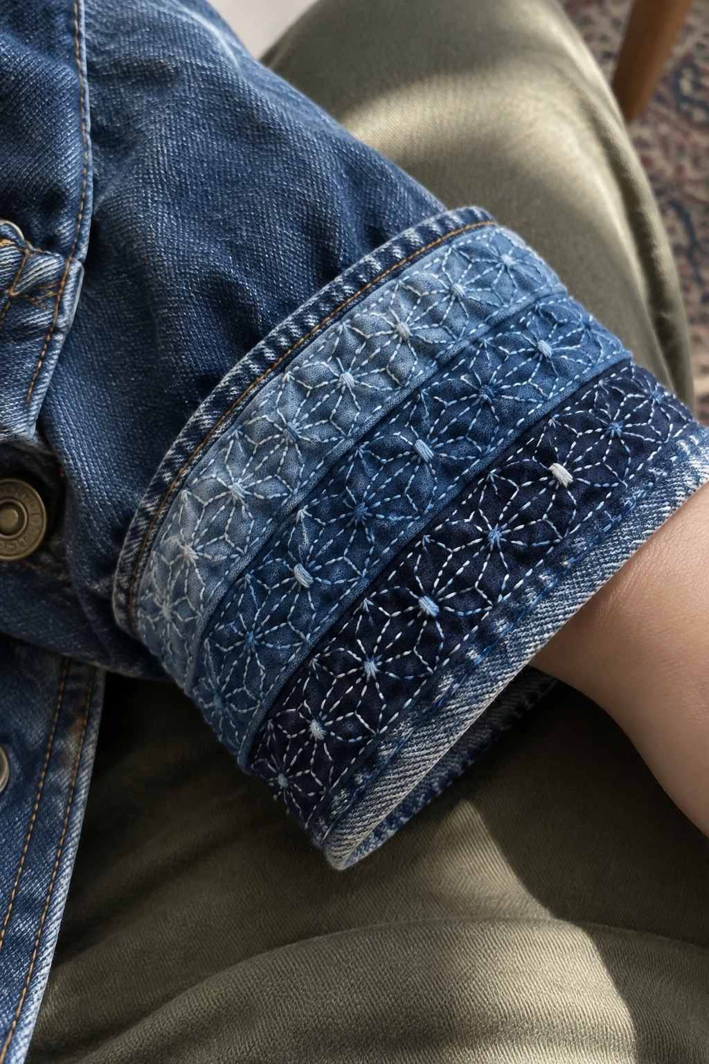 A denim jacket cuff embroidered with rows of pale asanoha patterns in contrasting blue fabric.