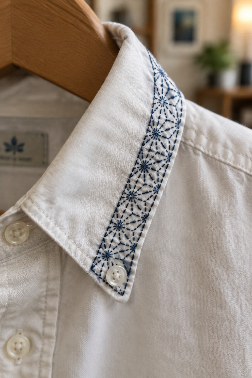 White shirt on a wooden hanger with a navy asanoha-stitched band along the collar.