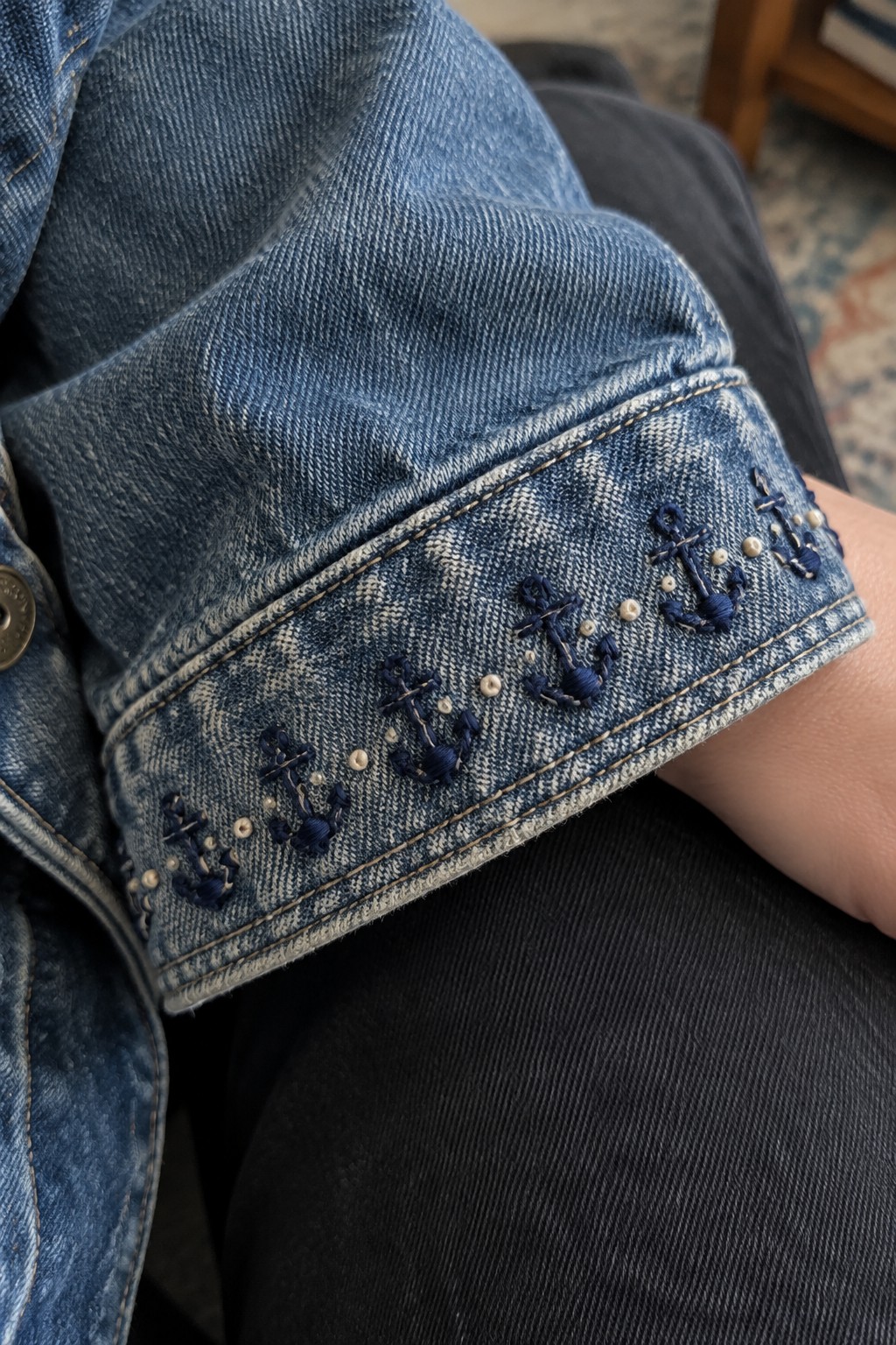 Close-up of a denim jacket cuff embroidered with dark blue flowers and small pale beads.