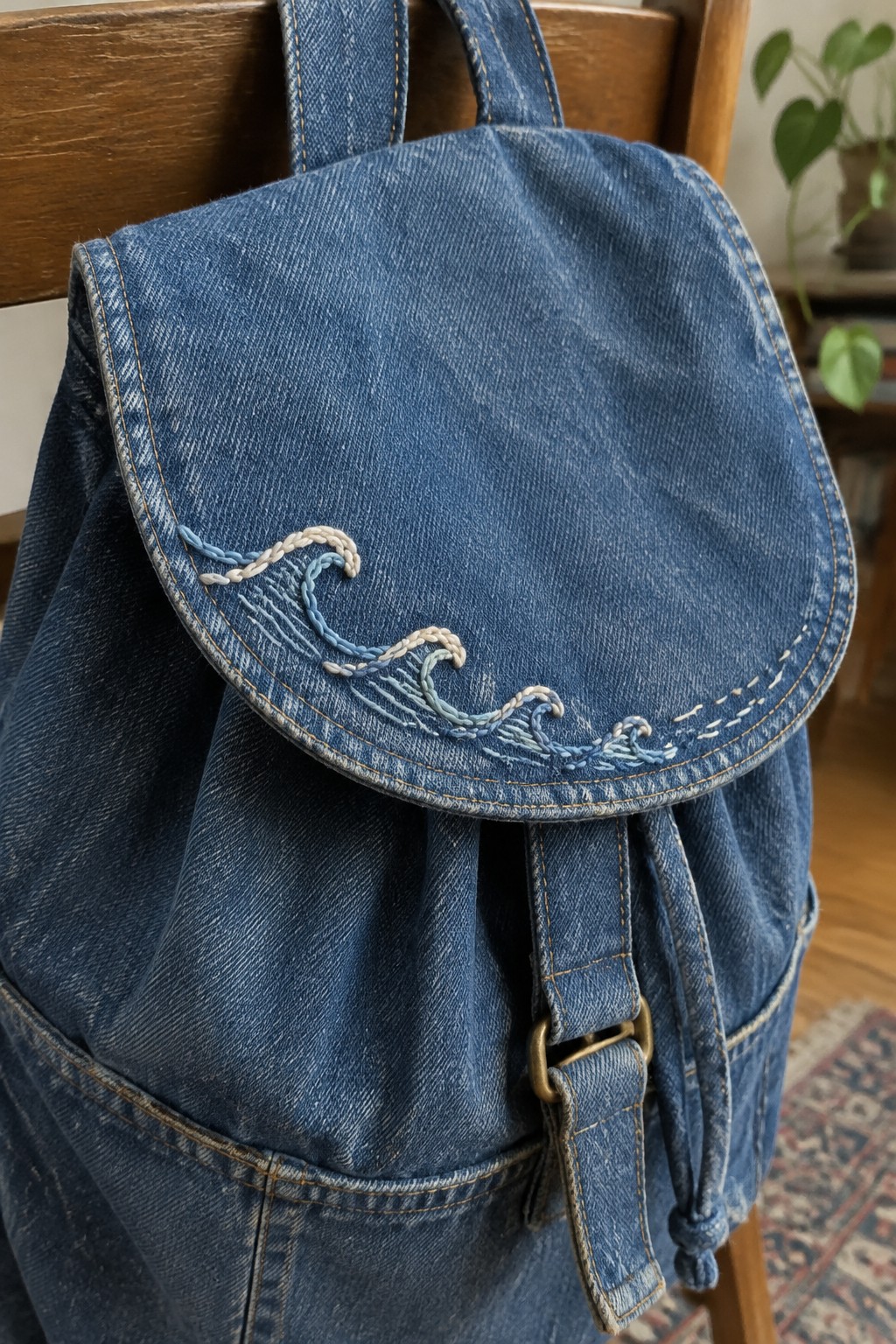 A blue denim backpack with a blue-and-cream embroidered wave along the curved flap.