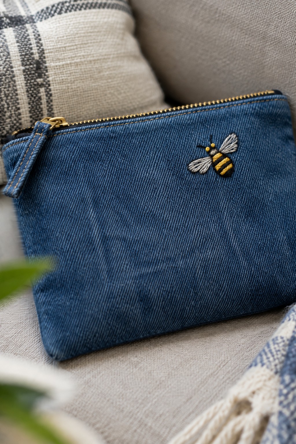A blue denim zip pouch with a small embroidered yellow-and-black bee and pale wings.