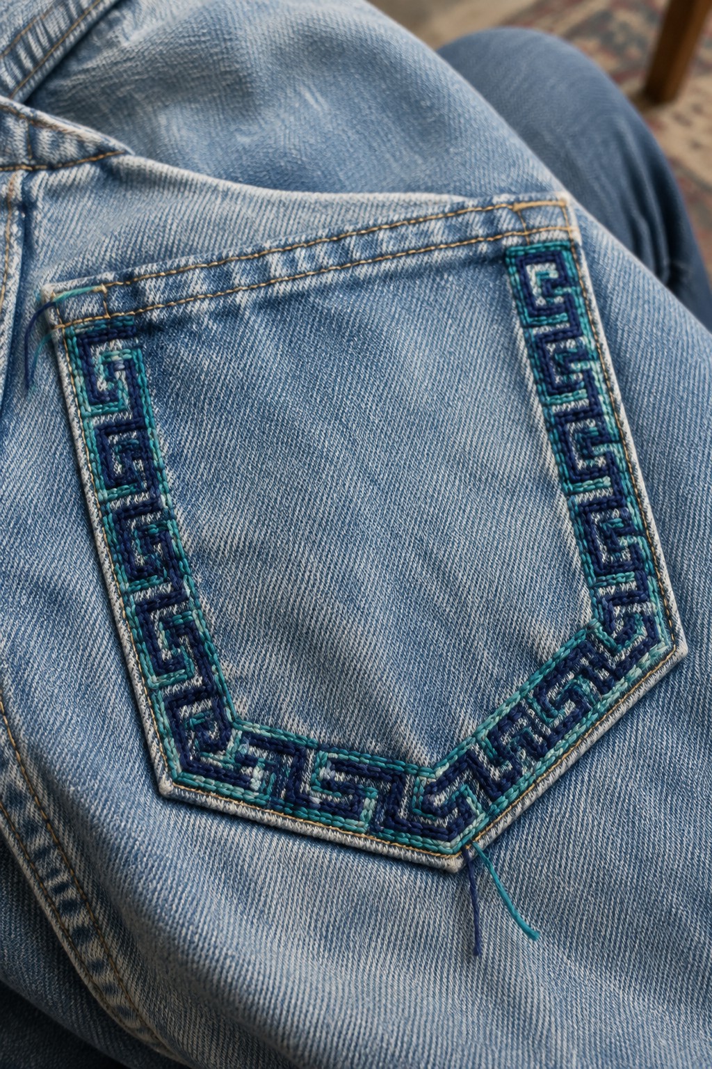 Blue and teal geometric embroidery outlines a large pocket on faded denim.