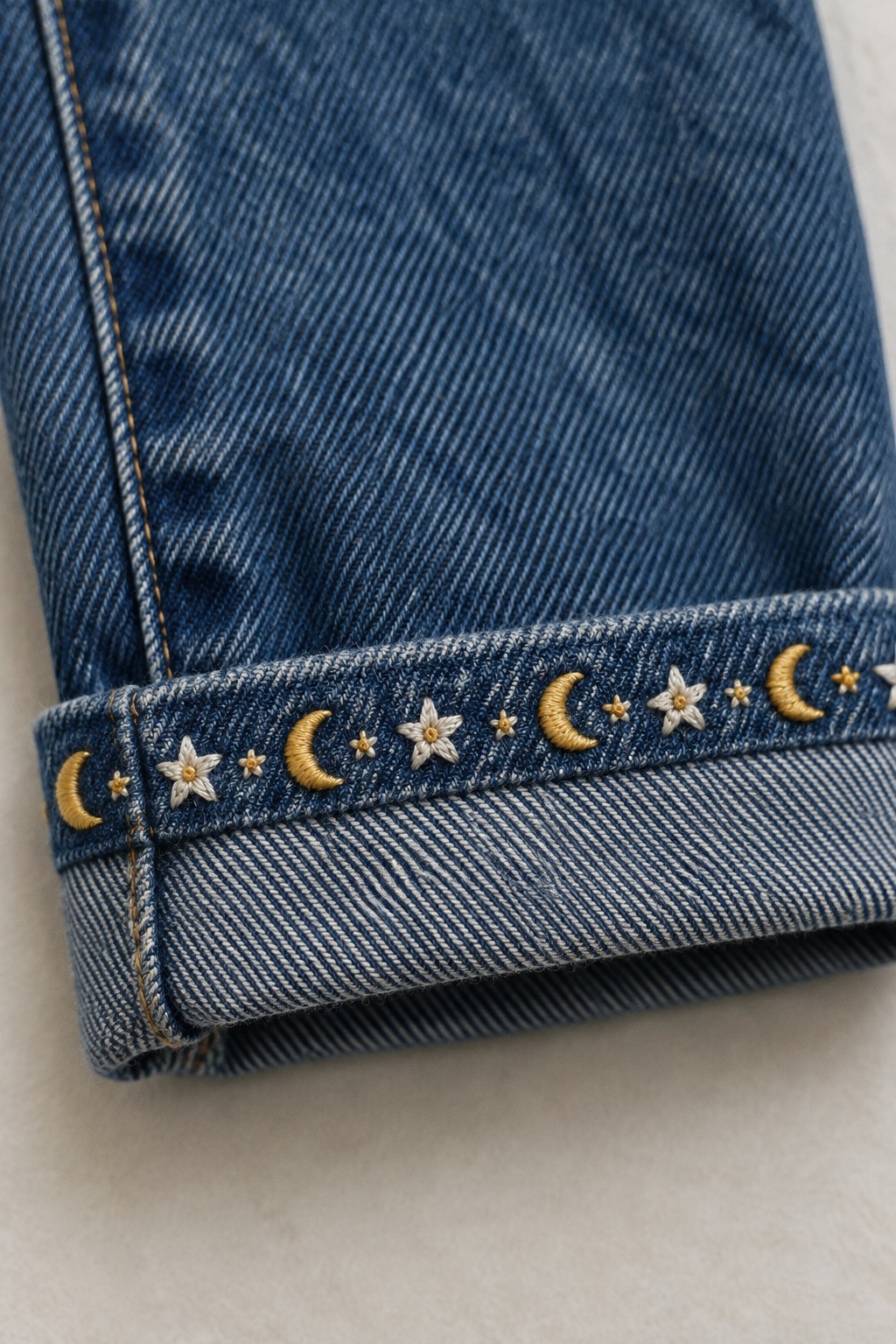 Gold crescent moons and cream stars are embroidered along the folded cuff of blue denim.