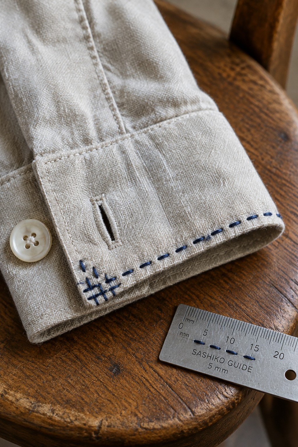 Beige fabric cuff with blue running stitches beside a Sashiko spacing guide on a wooden surface.