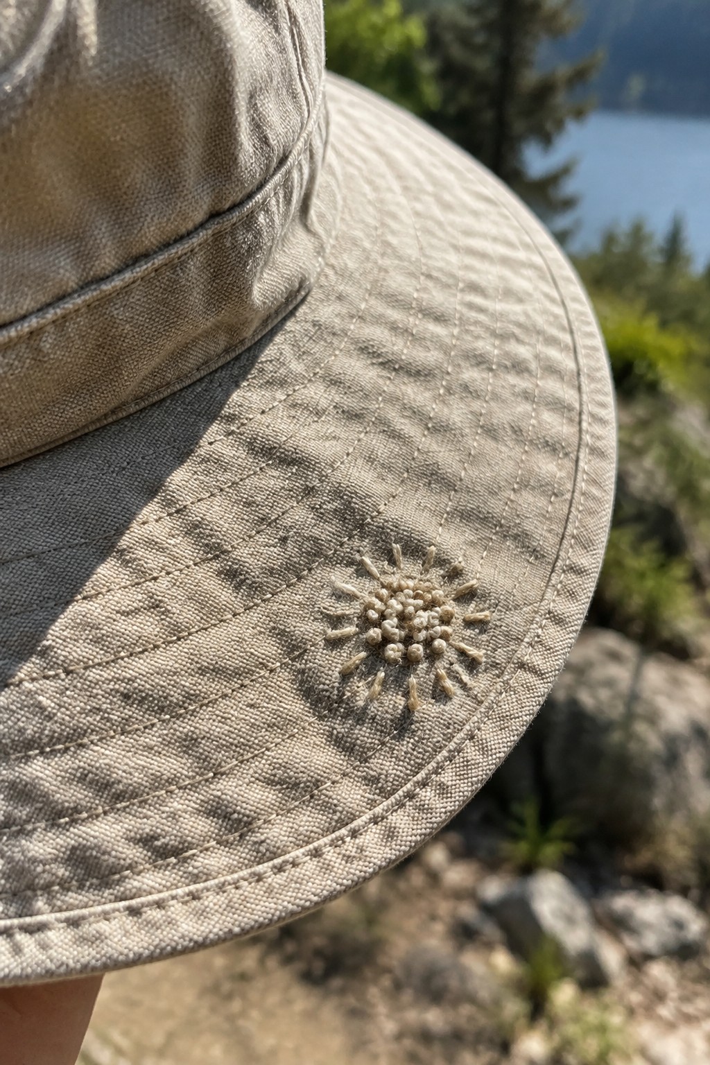 A small cream-colored embroidered flower decorates the brim of a beige sun hat.