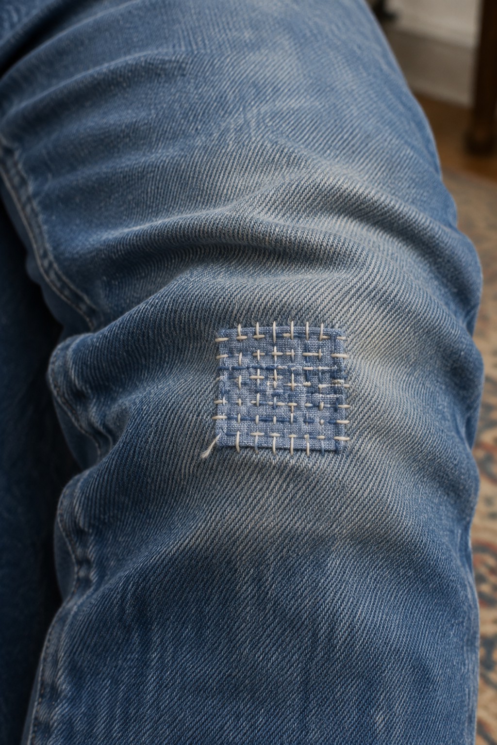 A small square grid of pale stitches reinforces a worn spot on blue denim.