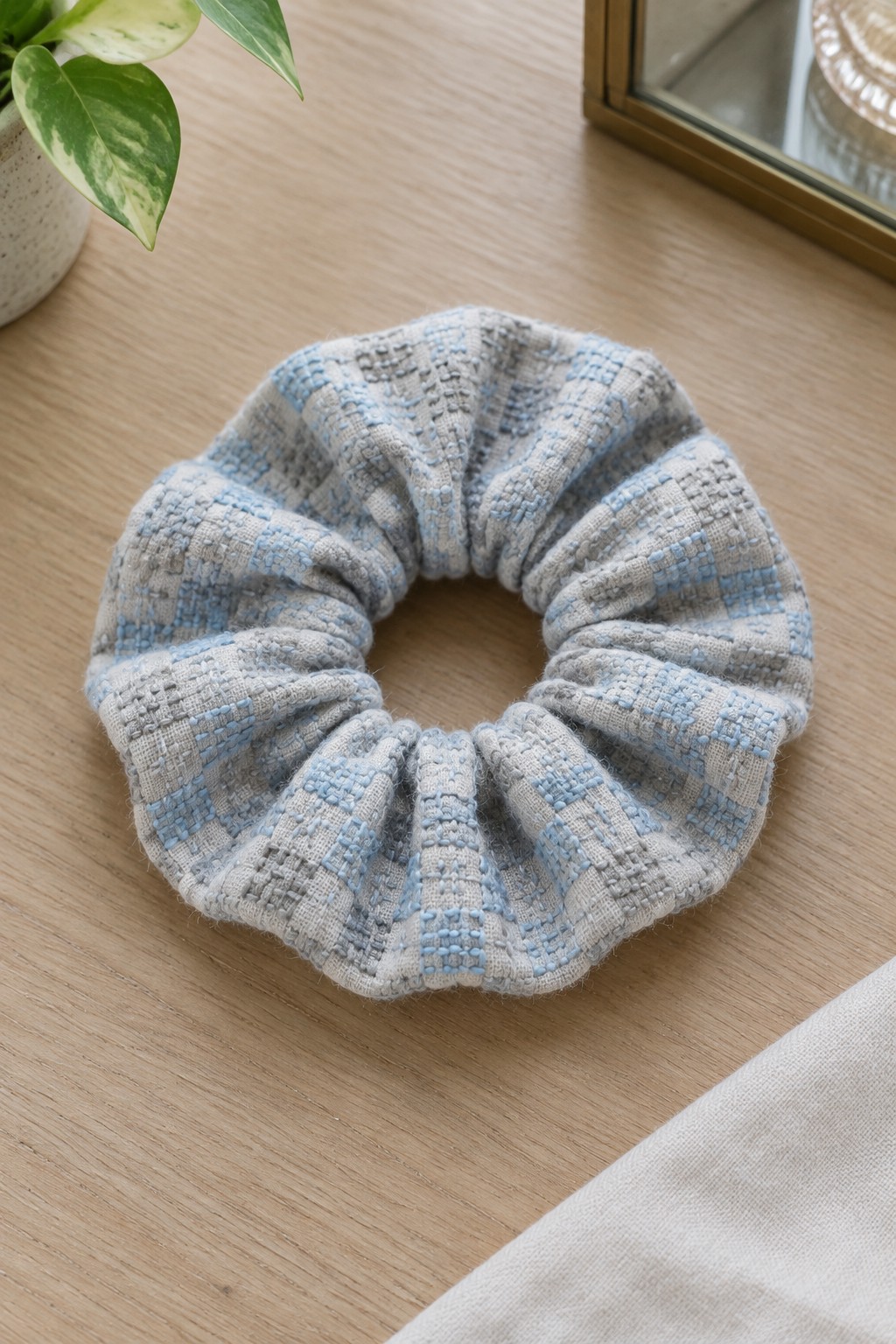 A gathered blue-gray patterned fabric scrunchie rests on a wooden table beside a potted plant.