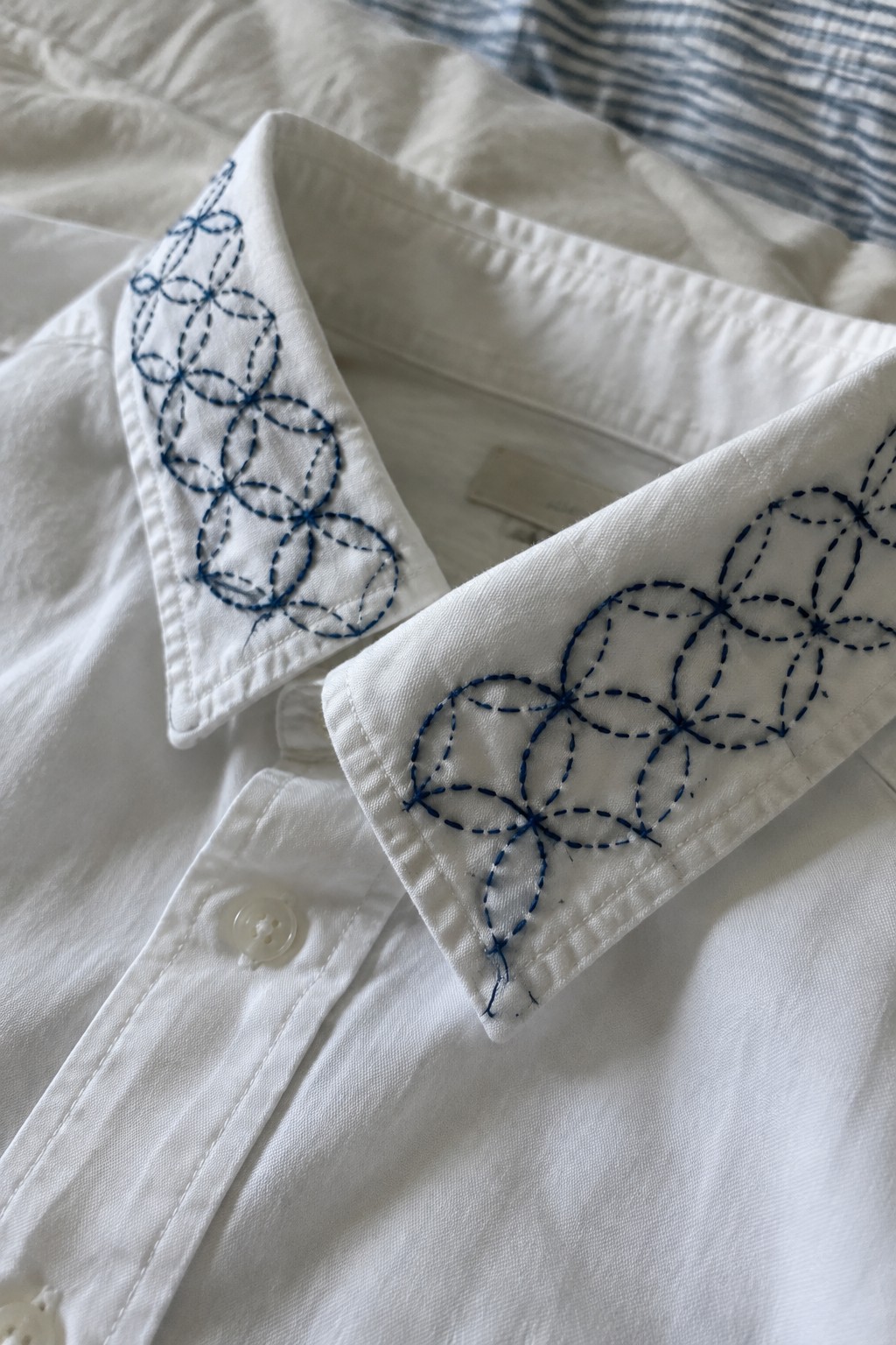 White shirt with blue sashiko circle embroidery stitched along both collar points.