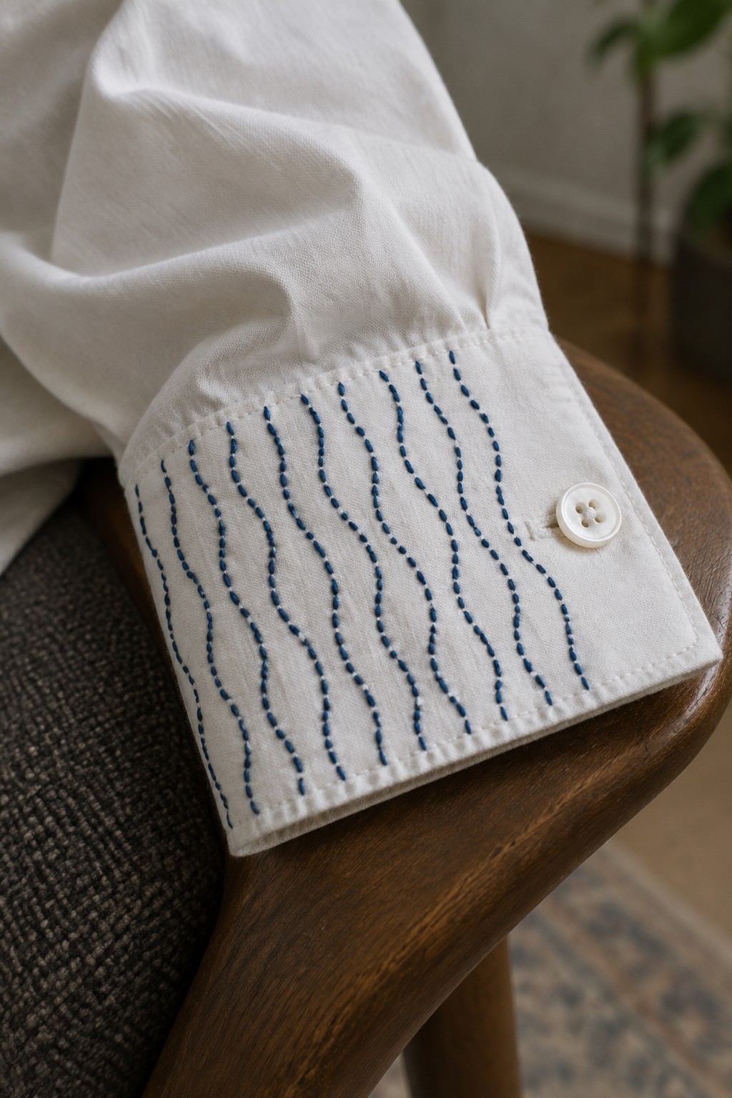 White shirt cuff embroidered with wavy blue lines and fastened with a white button.