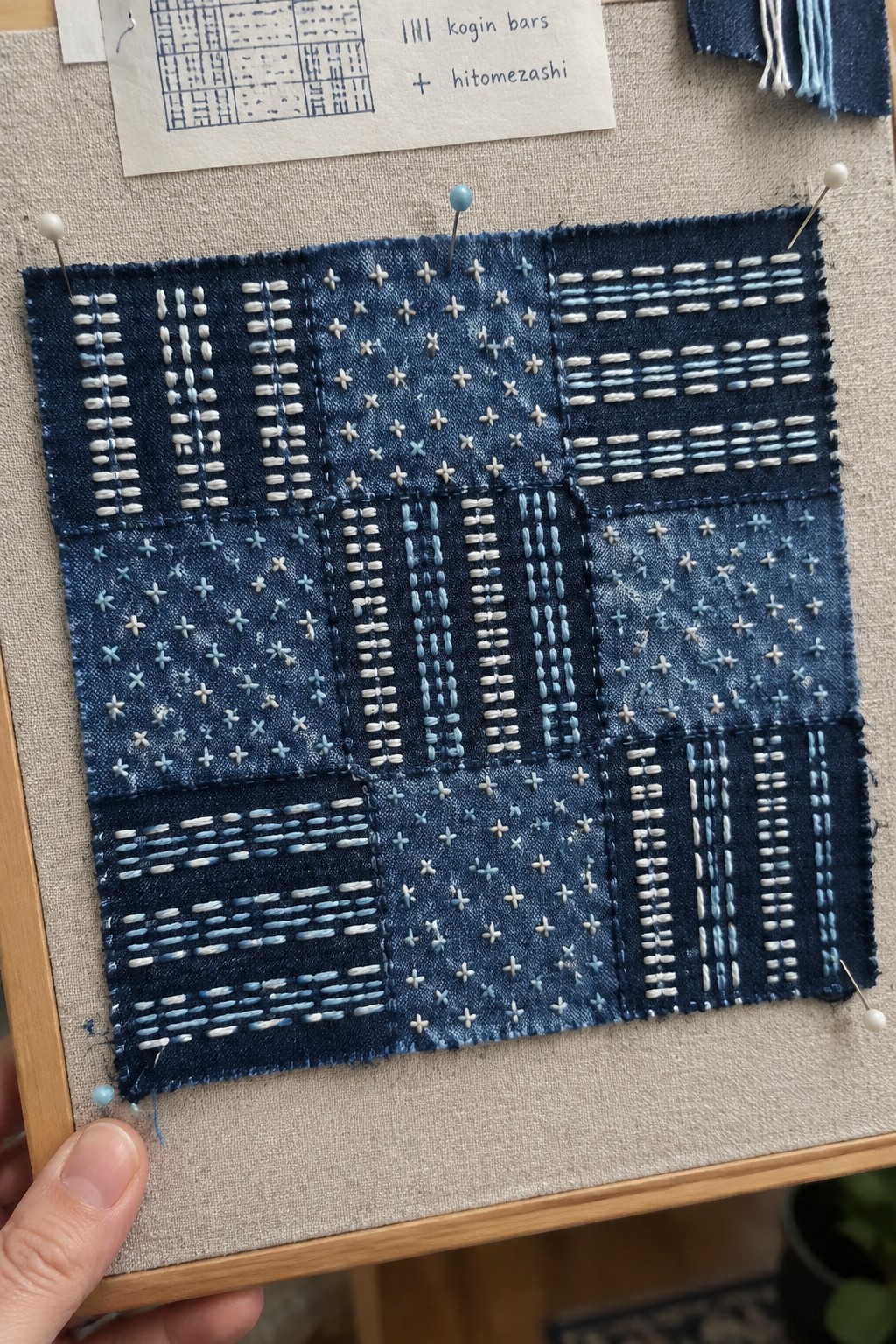 Indigo fabric sampler divided into blocks of white and pale blue bars and small cross-shaped stitches.
