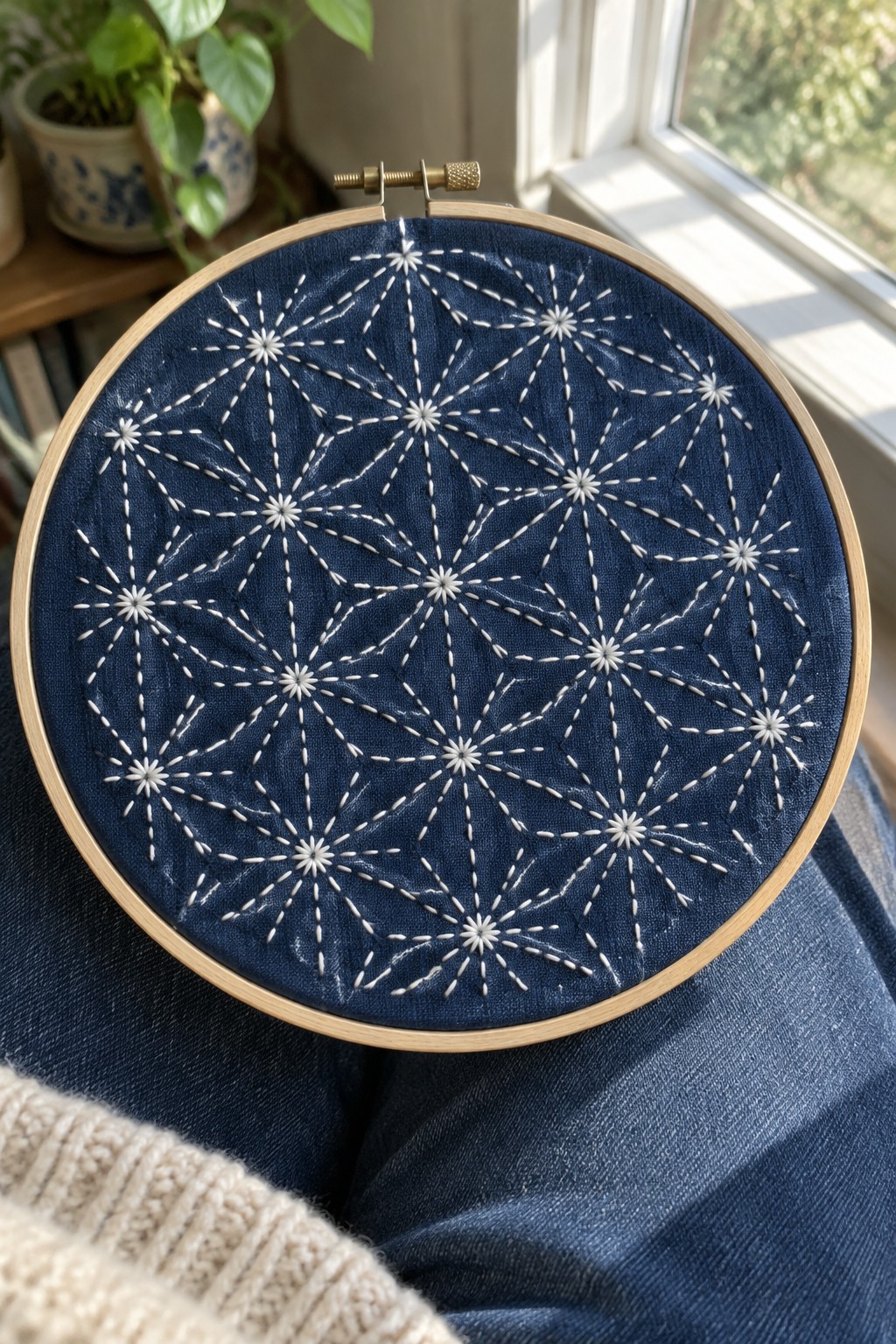 White geometric starburst stitching covers dark blue fabric held in a wooden embroidery hoop.