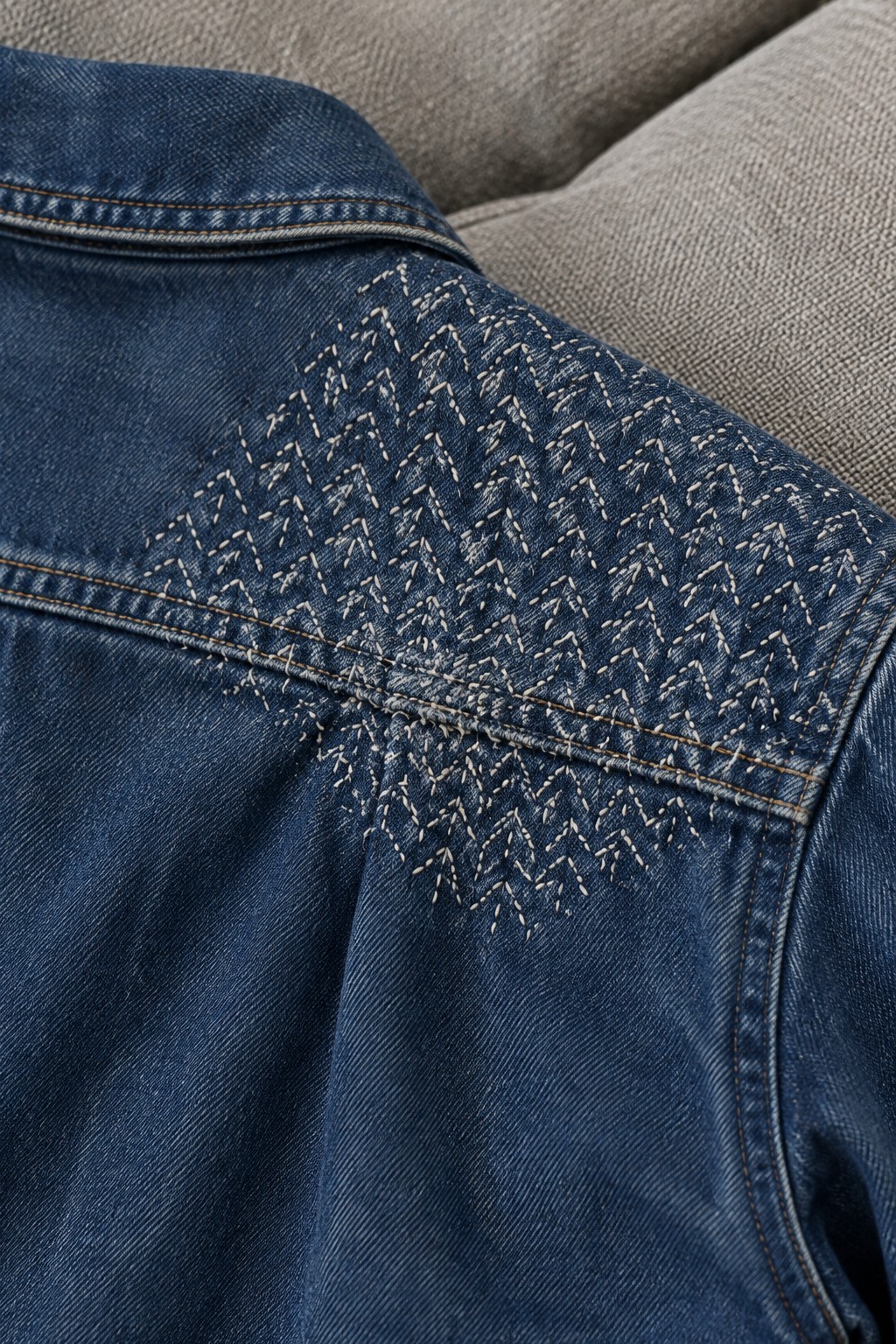 Pale chevron embroidery covers part of the back yoke on a blue denim jacket.
