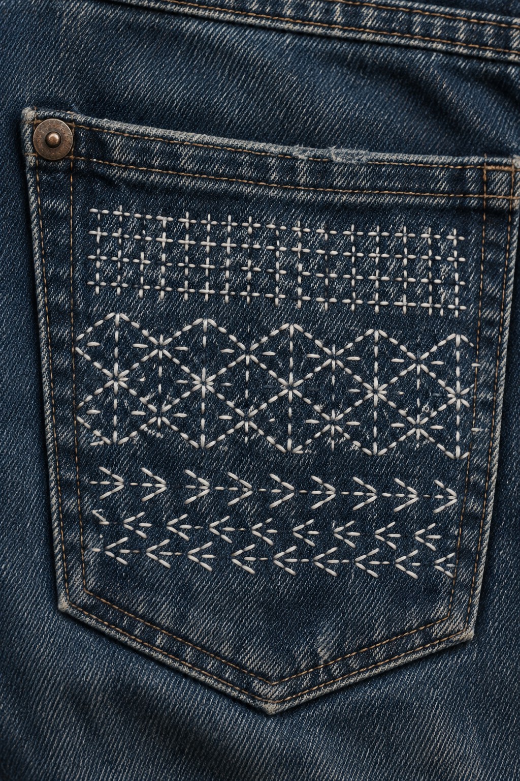 Pale geometric embroidery in rows decorates a dark denim pocket.