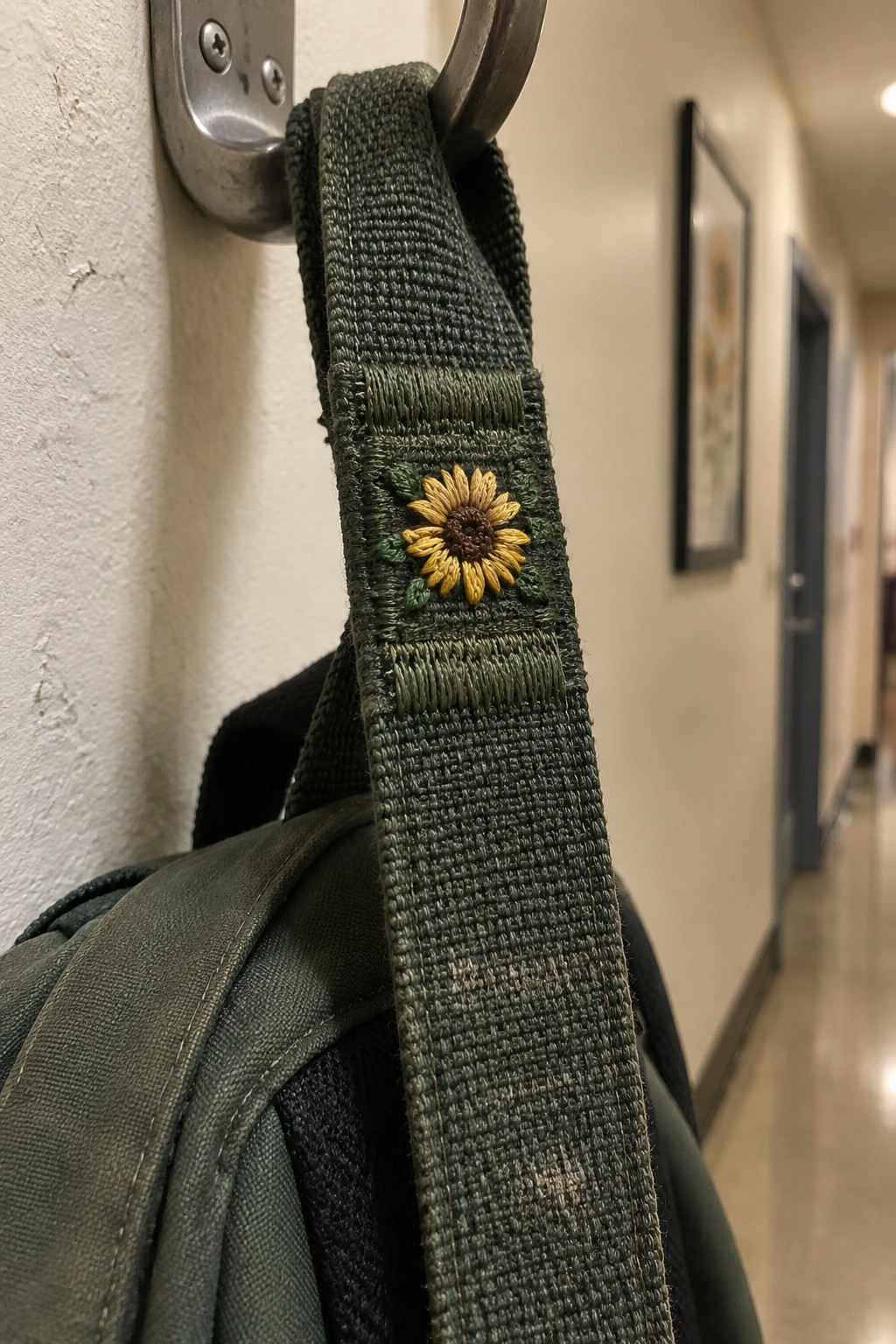 A dark green backpack hangs from a wall hook, with a small yellow sunflower embroidered on its strap.