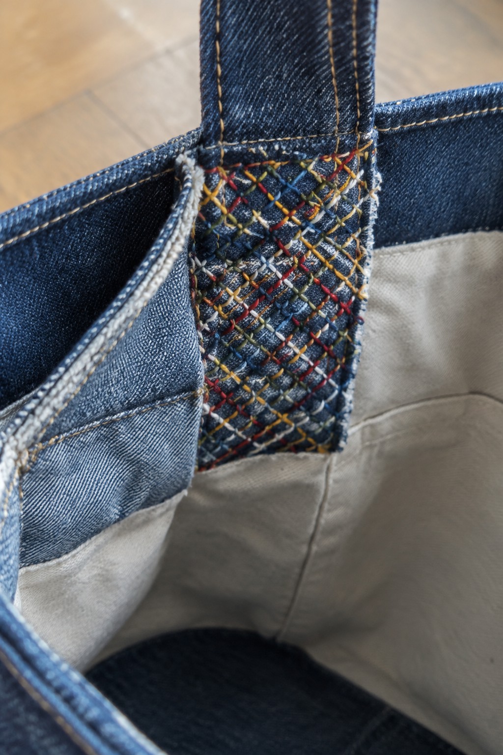 Close-up of colorful crosshatched stitching reinforcing a denim tote handle attachment.
