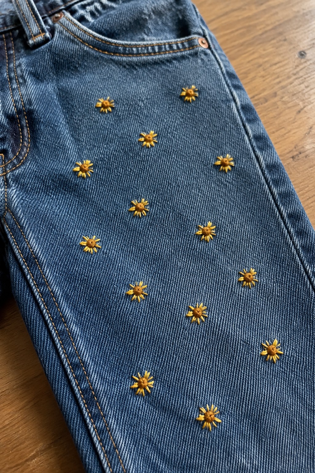 Small yellow embroidered flowers are scattered across the leg of blue jeans.