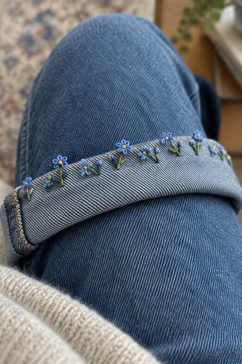 Small blue flowers with yellow centers are embroidered along the turned-up cuff of blue jeans.