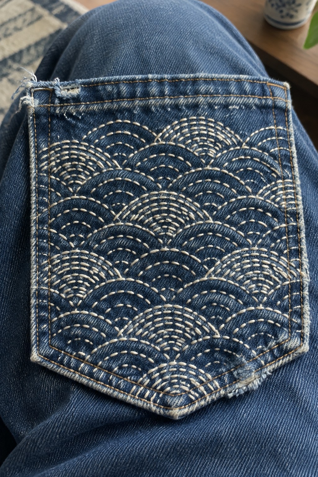 Cream repeating wave embroidery covers the back pocket of blue jeans.