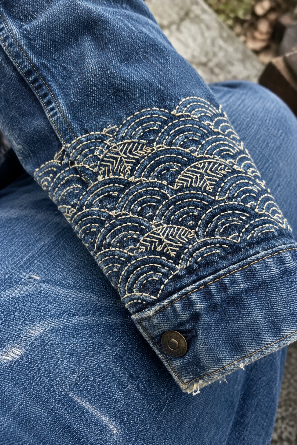 Pale repeating wave embroidery decorates the sleeve and cuff of a blue denim jacket.