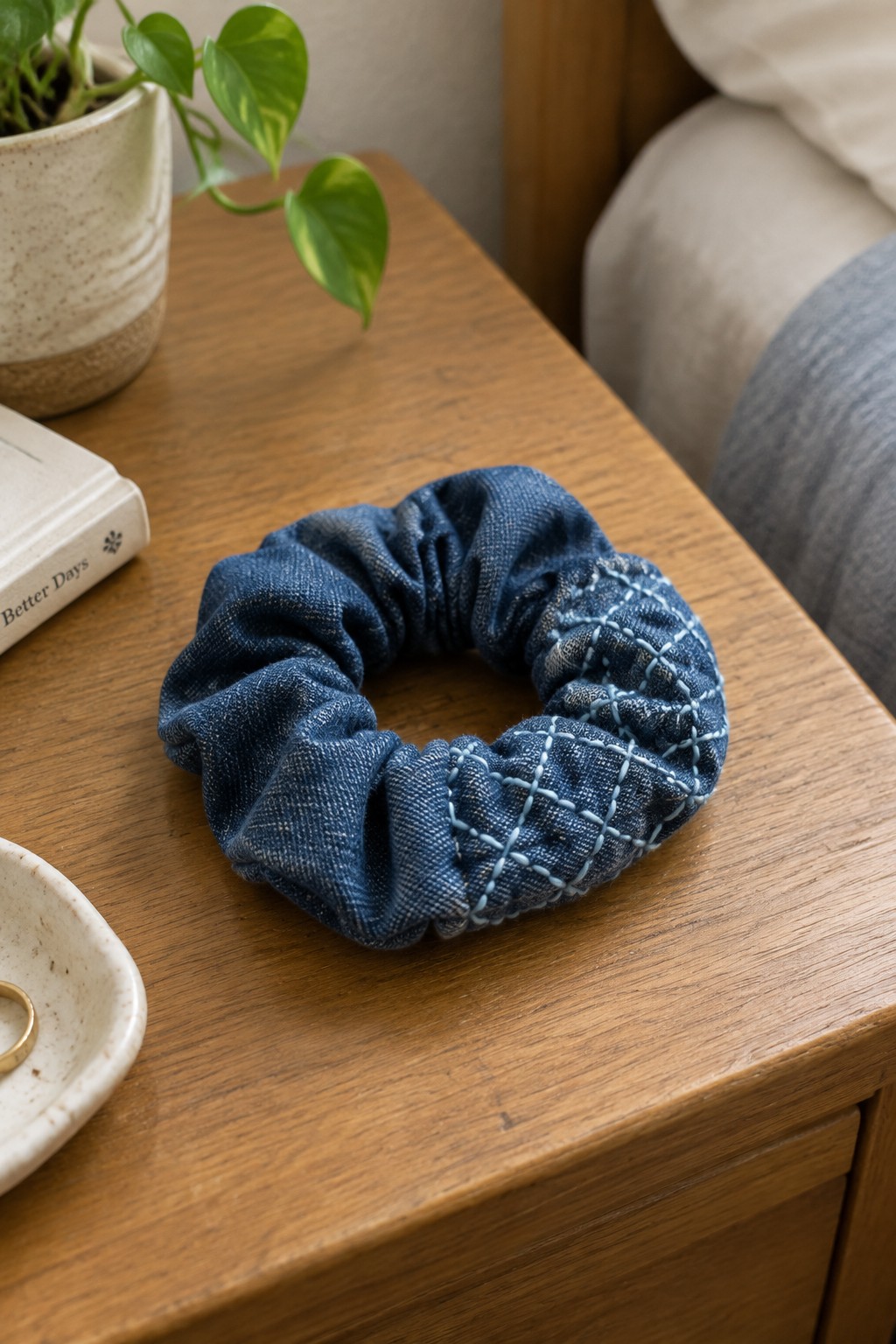 A dark blue denim scrunchie with pale sashiko-style stitching rests on a wooden bedside table.