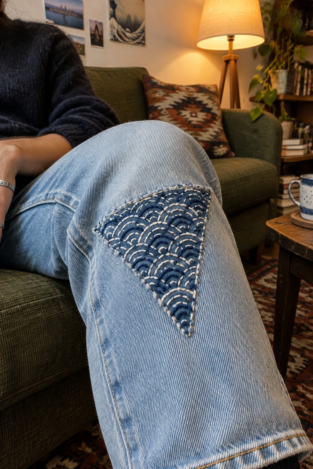 Light blue jeans with a dark blue triangular knee patch stitched in curved rows of pale thread.