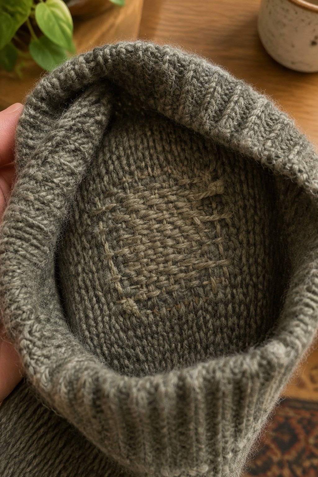 Close-up of a gray-green knitted sweater with a woven darn inside the cuff.