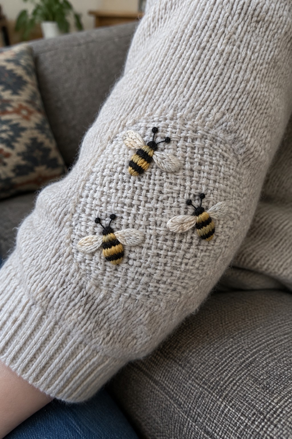 Three yellow-and-black embroidered bees decorate a woven repair on the elbow of a cream sweater.