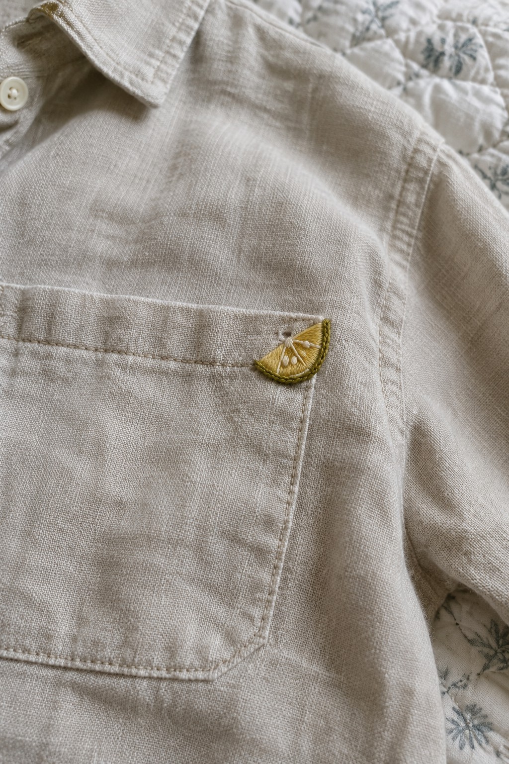 A small yellow embroidered lemon slice sits near the upper corner of a beige shirt pocket.
