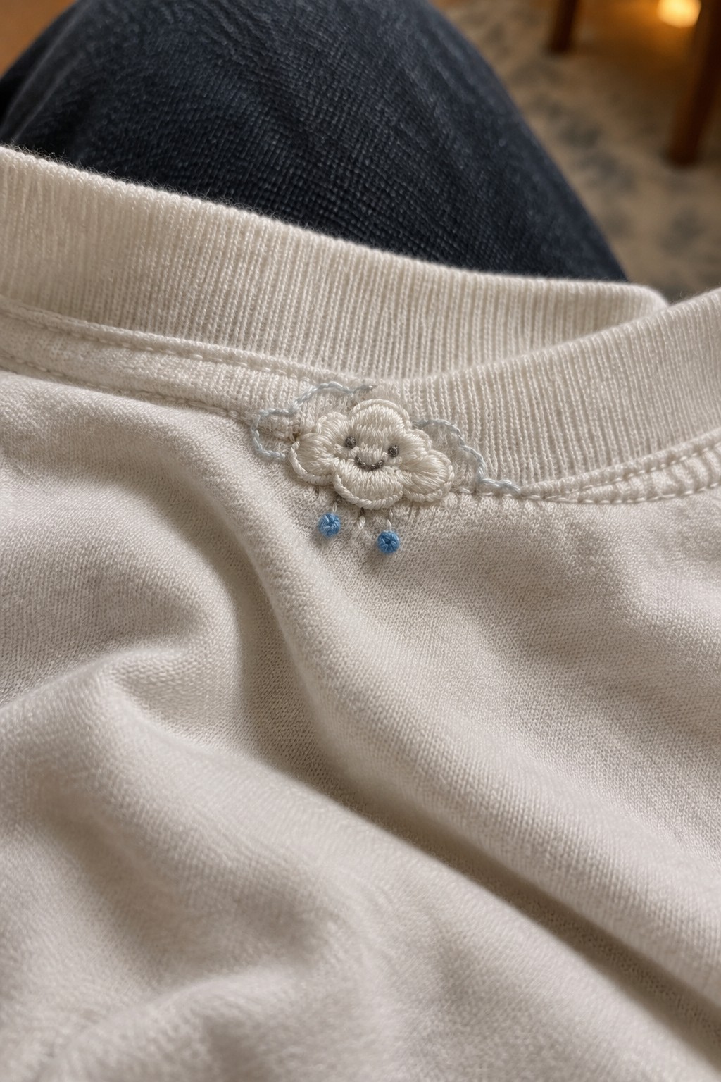 A small embroidered white flower with blue accents sits below the ribbed neckline of a white shirt.