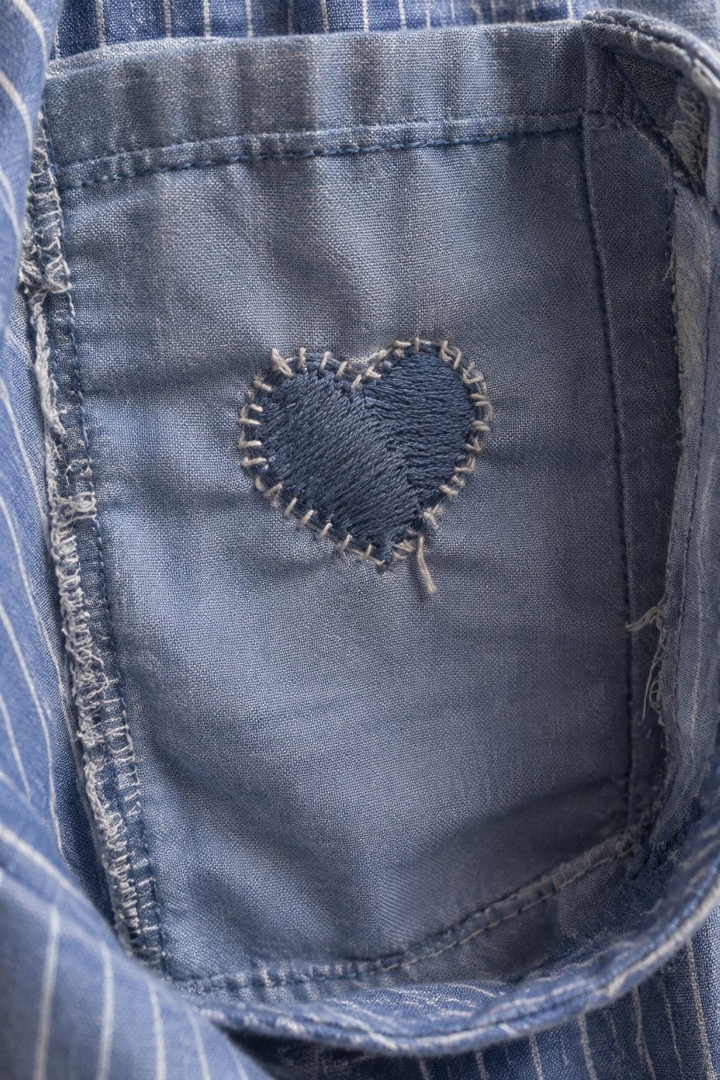 A dark blue embroidered heart with pale border stitches covers a small hole in blue shirt fabric.