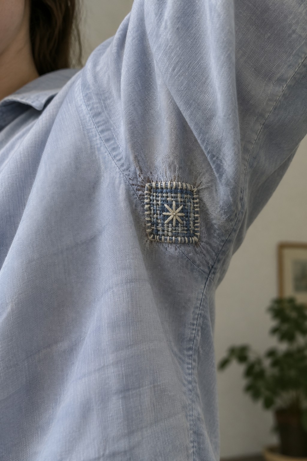 A square blue and cream woven patch with a star covers a frayed area beneath the raised arm of a light blue shirt.